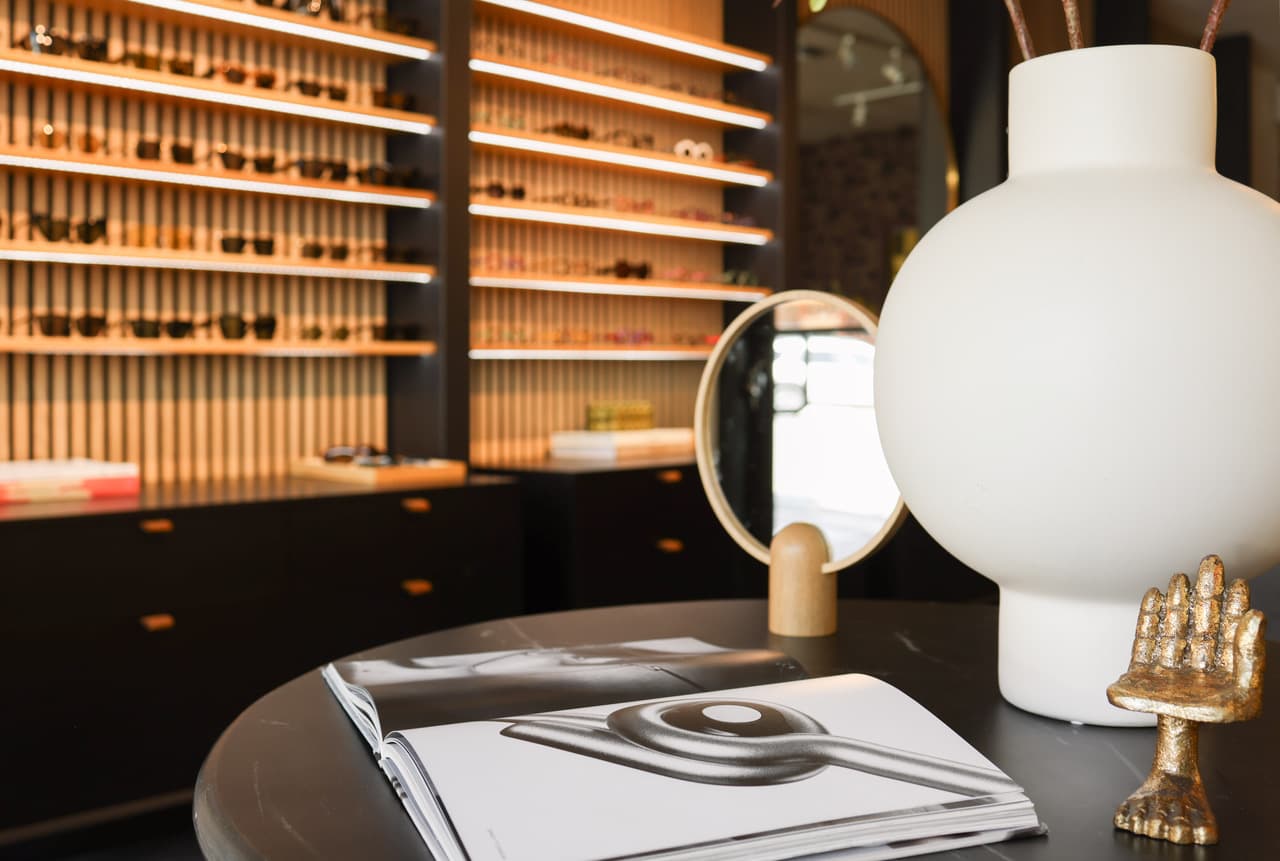 A stone table with a white vase, a small brass sculpture, and an open magazine, with shelves of frames softly out of focus behind.