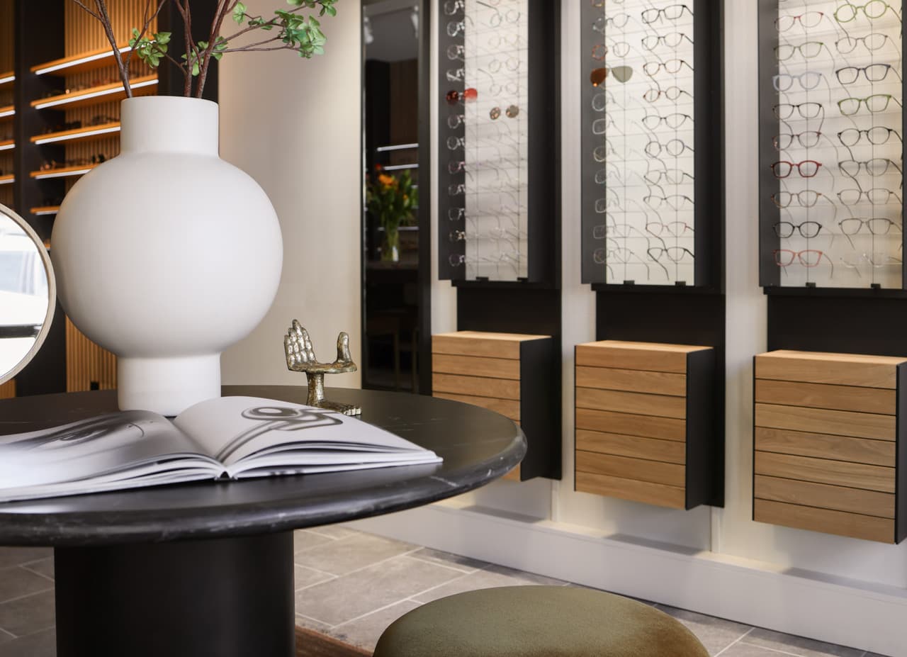 The fitting area: a round stone table with an open book and vase, an olive stool, and wall cases of frames alongside.